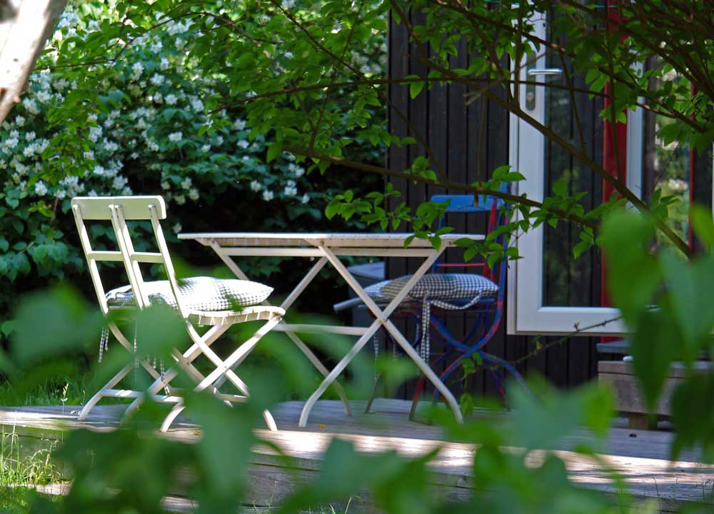 Table and chairs with cushions set out in a shady area of a garden.