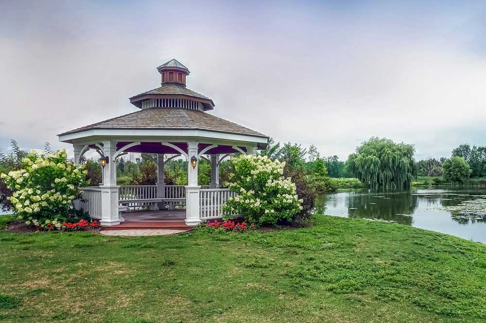 Hexagonal wooden gazebo on lawns next to a lake.