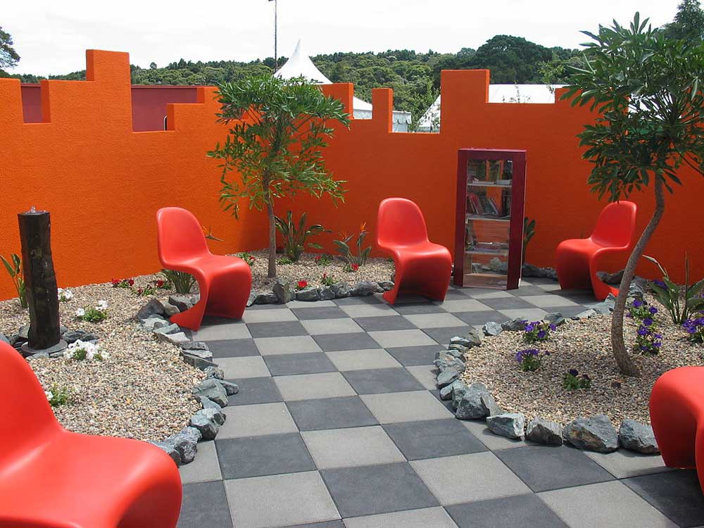 Modern garden display with orange chairs on checkered patio surrounded by orange walls.