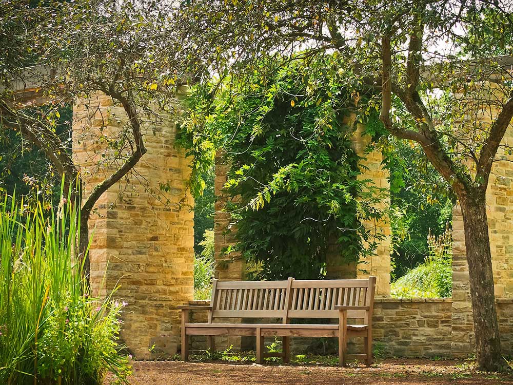 Wooden garden bench sitting among stonework and greenery.