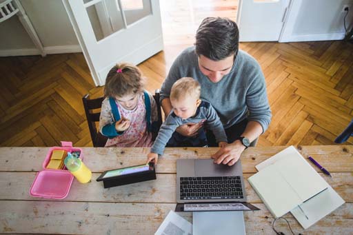 This is a photograph of a man and two children using a tablet and laptop.