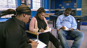 A photograph of two women and a man sitting together in an office environment, each writing notes.
