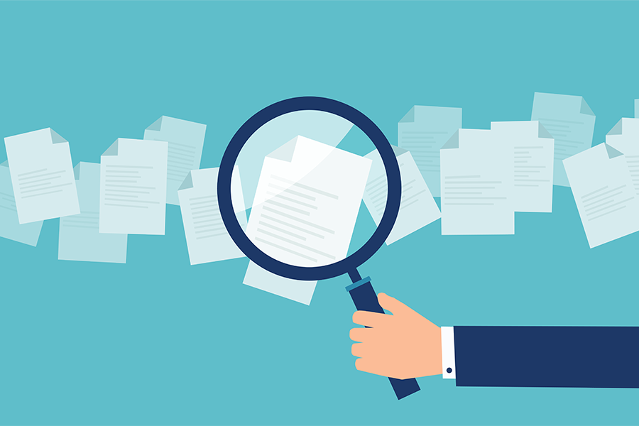 Une main tenant une loupe au-dessus de documents.