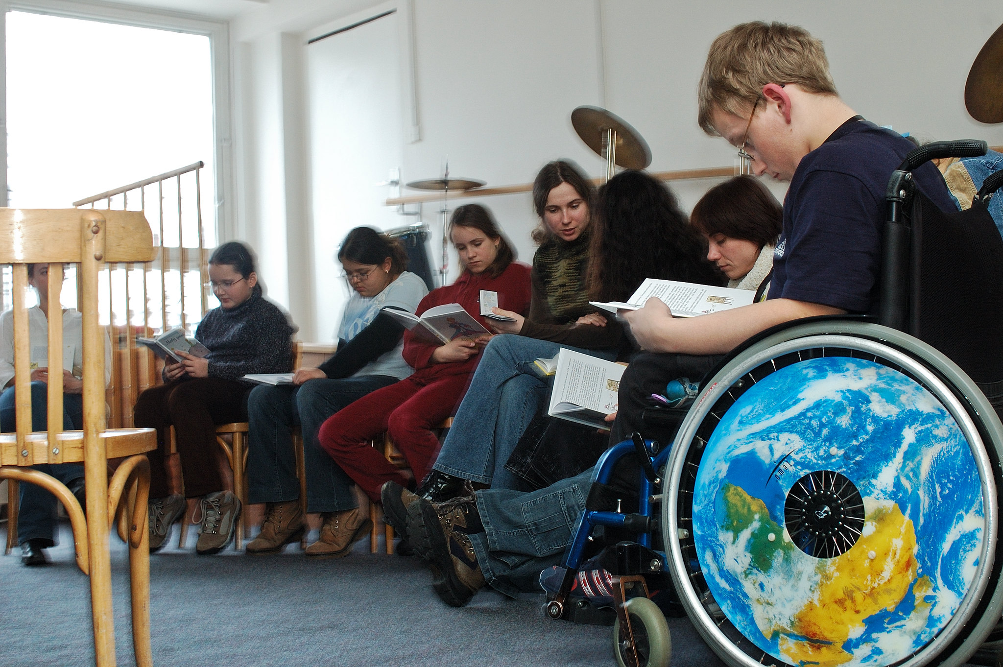 Photograph of a class reads from books. A disabled student is in a wheelchair