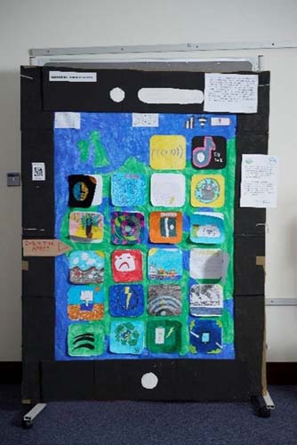 a large piece of artwork is shows that resembles a smartphone. On the “screen” are different apps with icons. Each app has a door that can be opened to reveal more information about issues relating to the impact of technology on the environment. The wallpaper for the screen is a map of Europe. There is a small sign that says “Open the apps!” and a sign showing the name “Lochardil Primary School”.
