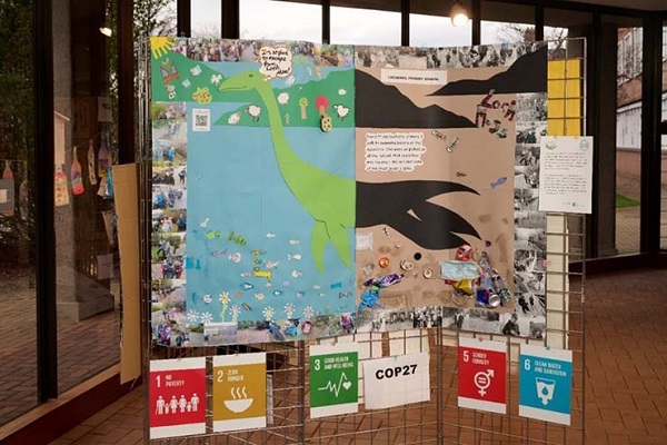 A collage is displayed on a metal frame with some of the SDGs in an open room. The collage features the Loch Ness monster split into two with one side representing how a healthy and happy Nessie might look in her natural environment and the other side showing a sad view, with collected rubbish included in the collage. Nessie is surrounded by photos of school pupils taking part in various outdoor activities around the Highlands area relating to sustainability.