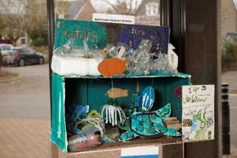 A 3D piece of artwork featuring recycled materials reworked into an underwater scene with various animals including turtles and jellyfish in various tones of blue and green. The surface of the water is covered in discarded plastic items. A slogan says “Be fantastic, recycle your plastic” and a small card reads “Muirtown Primary School”. Another card reads “14 Life below water” referencing the 14th SDG.