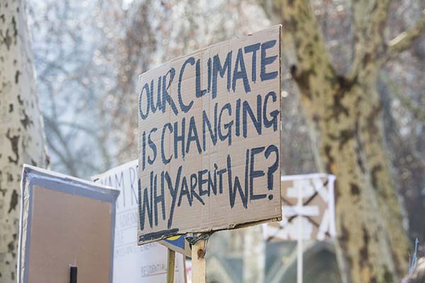 A cardboard protest placard saying ‘Our climate is changing, why aren't we?’