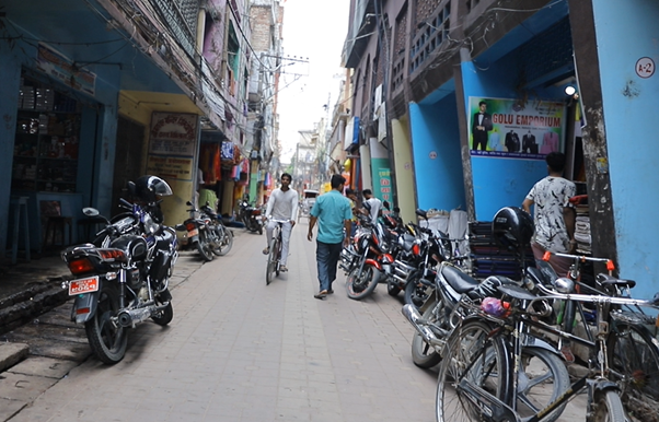 A narrow street in Nepal with bikes and motorbikes and people walking down with shop signs in different languages