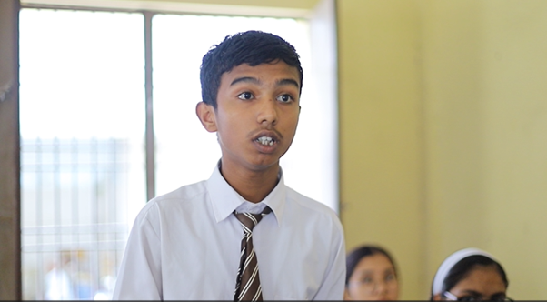 A boy in Nepal in school uniform standing up in class talking