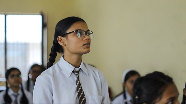 A girl in Nepal in school uniform standing up in class and talking