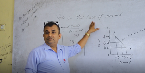 A male Nepali teacher pointing to a whiteboard with two languages on