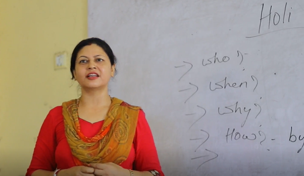 A female Nepali teacher standing in front of a whiteboard with English on
