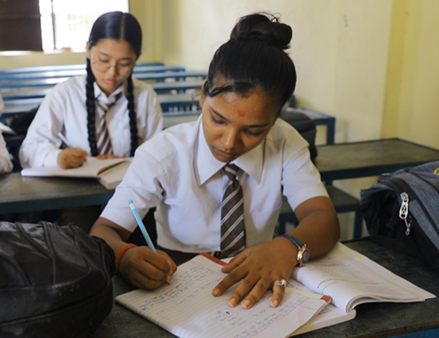 Two girls in a classroom in Nepal writing in their text books