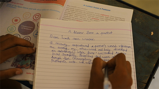 An exercise book over a text book with the hands of someone writing a letter in English