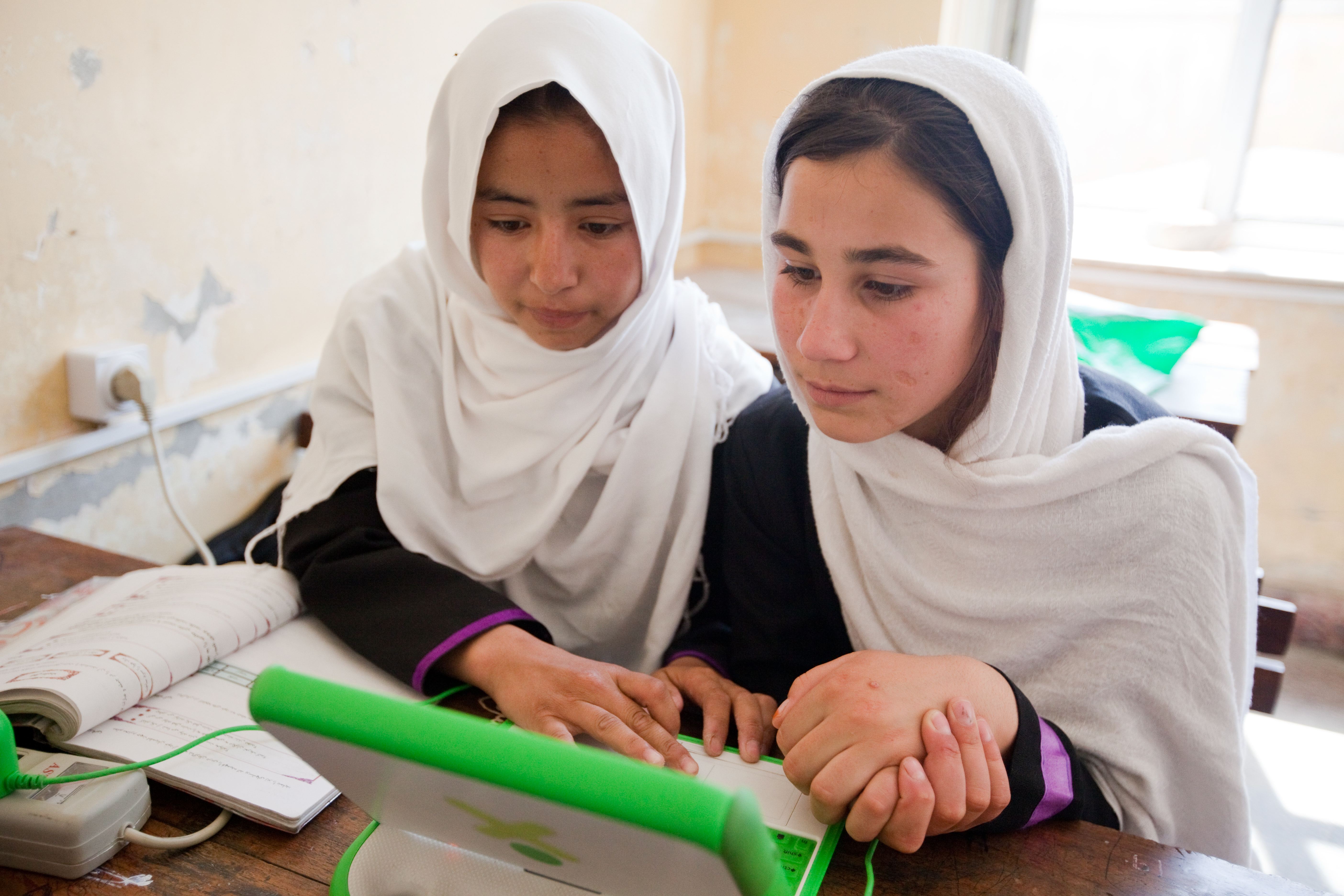 2 girls sitting in a school looking at a laptop
