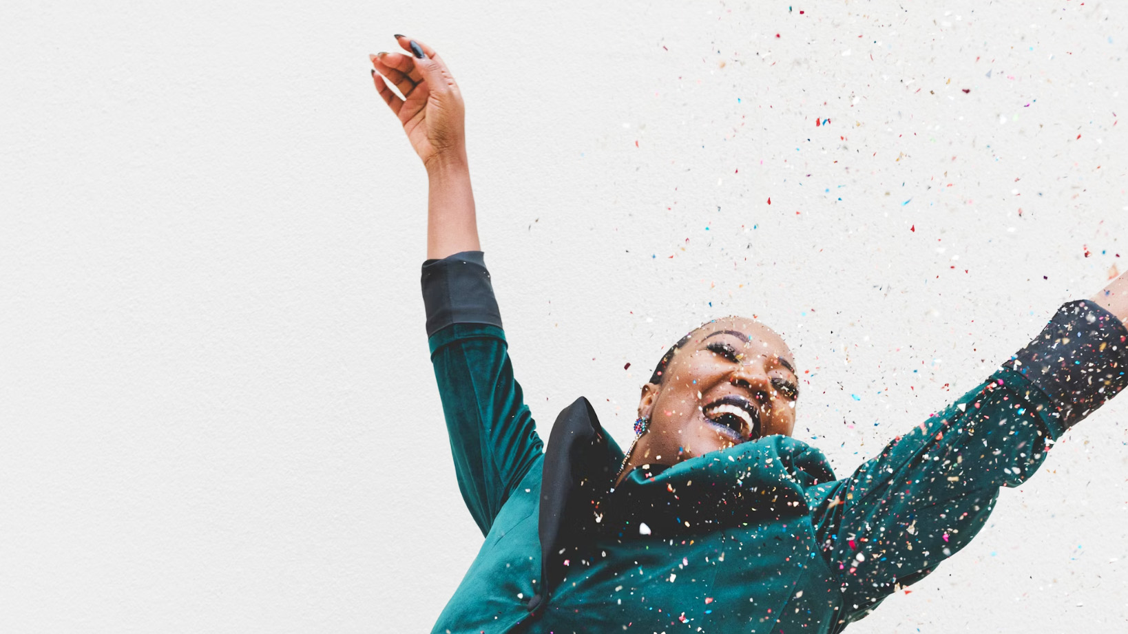 A female business owner is dancing and smiling with glitter falling on her.