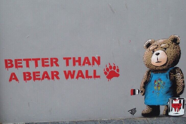 1.3	An artwork of a teddy bear painting the words ‘Better than a bear wall’ and a bear paw print onto a wall in red paint.