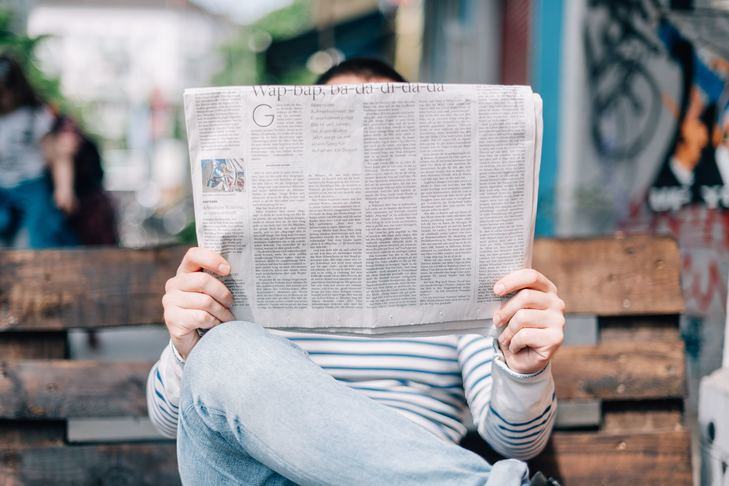 A photo of someone almost completely obscured by the large newspaper they are holding up in front of them.