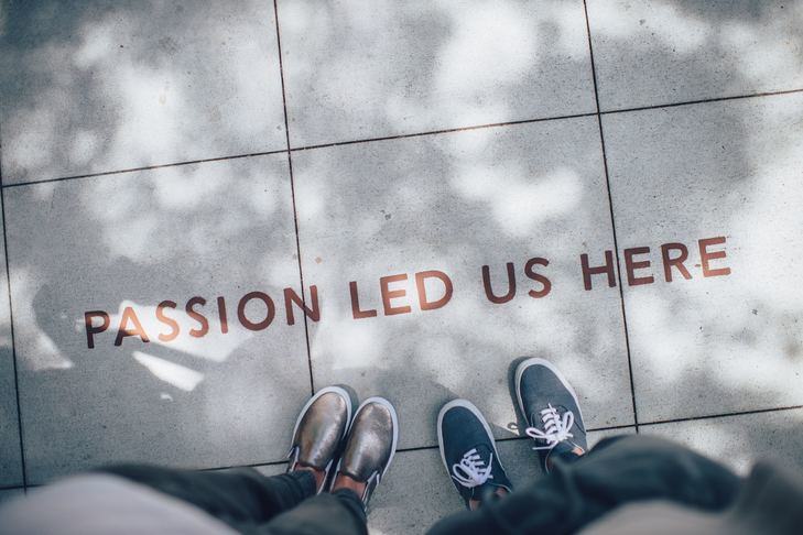 A photograph of paving slabs and the photographer's and another's feet. Written on the paving is 'Passion led us here'.