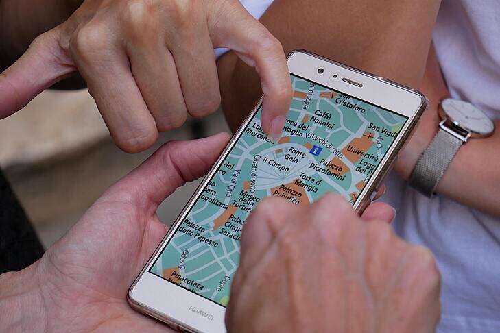 Someone points to a place on a map which is displayed on a smartphone held by someone else.