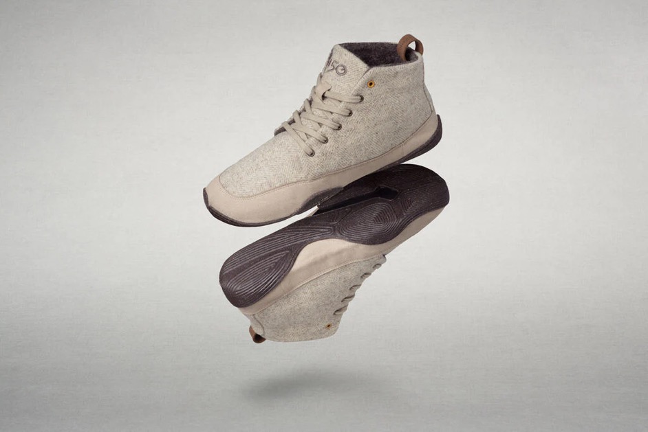 A pair of Wildling shoes in a neutral beige tone. The shoes feature a textured fabric upper, flexible dark brown soles, and subtle lace detailing. The image shows the shoes floating against a plain light gray background, highlighting their lightweight construction and natural aesthetic.