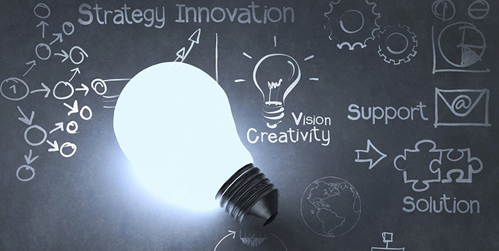 A lit lightbulb reflecting against a blackboard with various diagrams and drawings on it. Words like creativity, support and solution are also written on it.