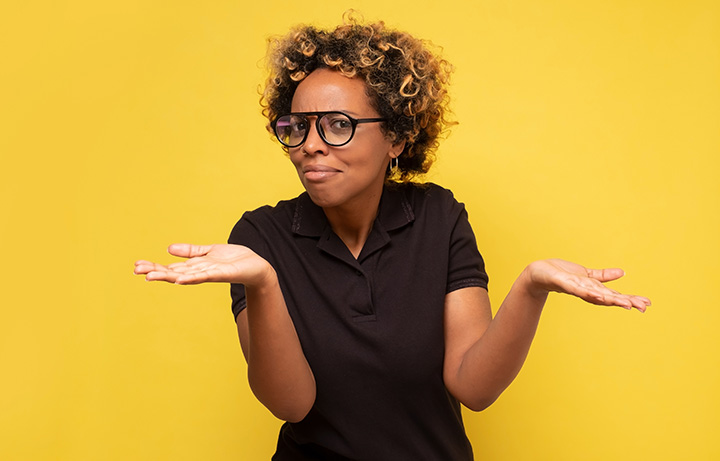 A young black woman dressed in a black dress, with her hand outstretched shrugging. She has a questioning expression.