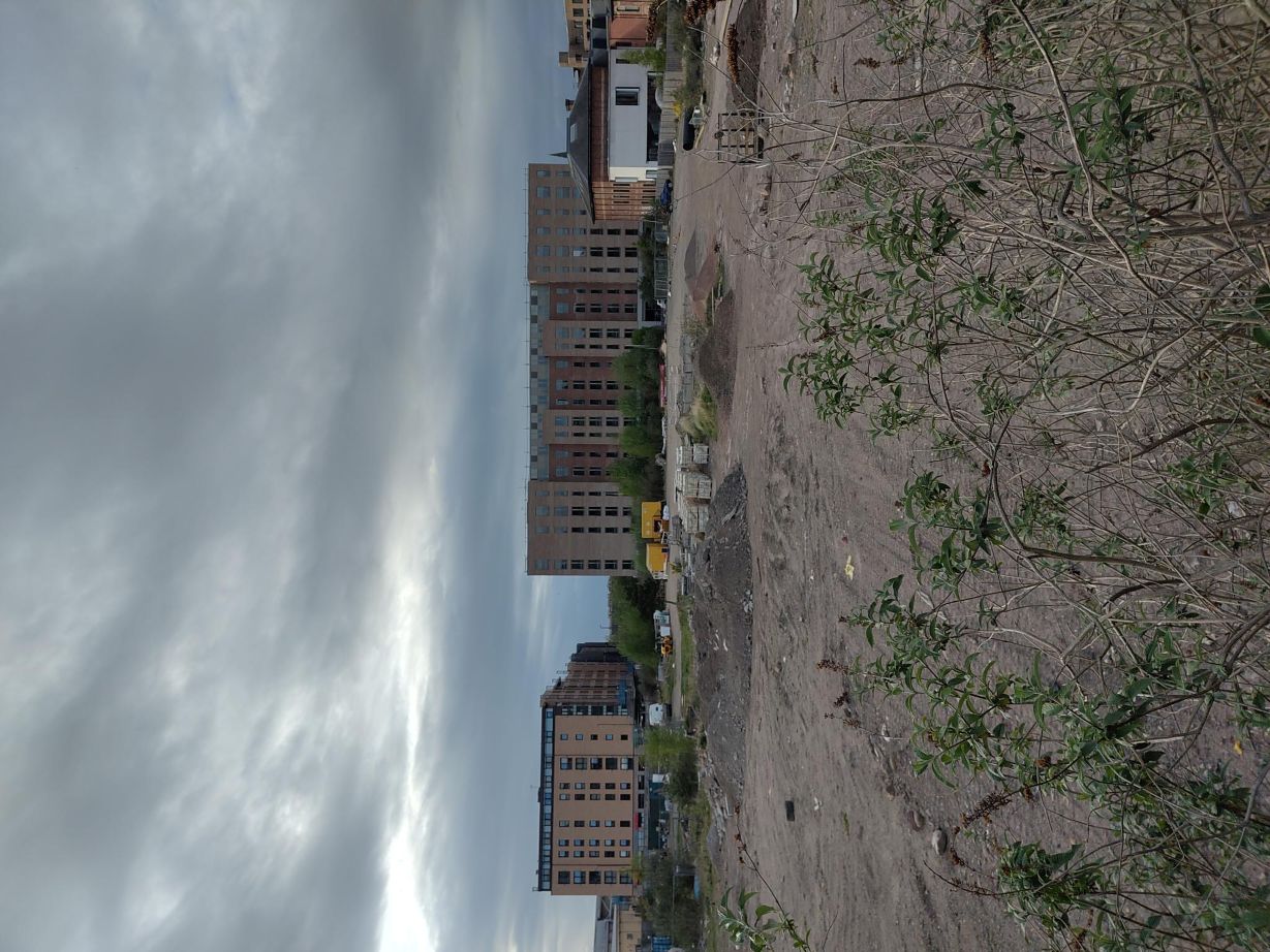 Two modern office or residential blocks to the rear, with a multi-hectare, cleared, building site, in the foreground.