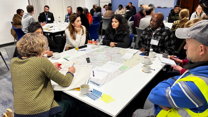 A table of 7 people in conversation, various genders and ethnicities. Another three similar tables in the background