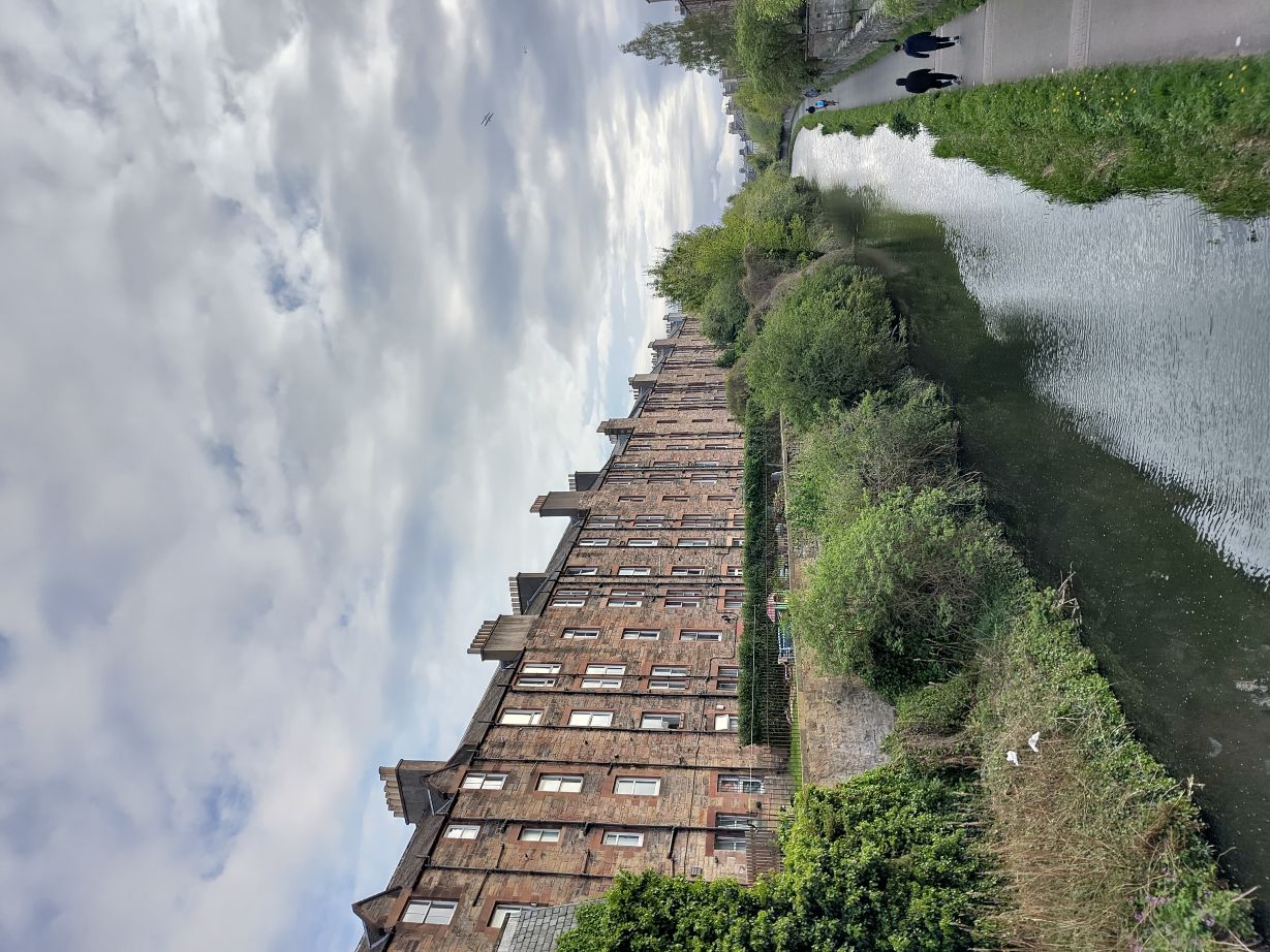 4 floor tenements on the left. Their gardens end with a high wall that drops down, through trees, to a canal and footpath