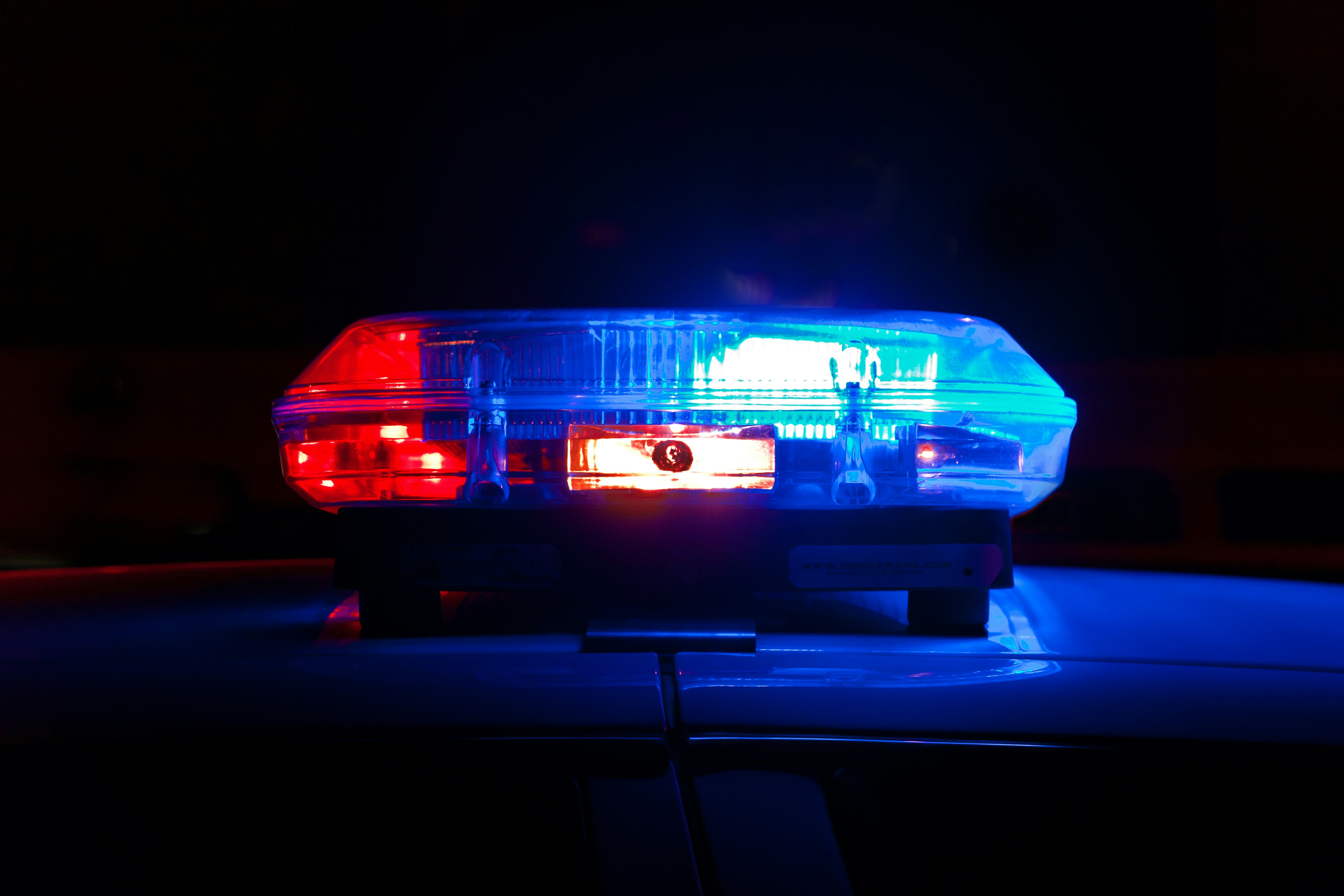 An up close image of police lights lit up on the top of a police car against a black back drop