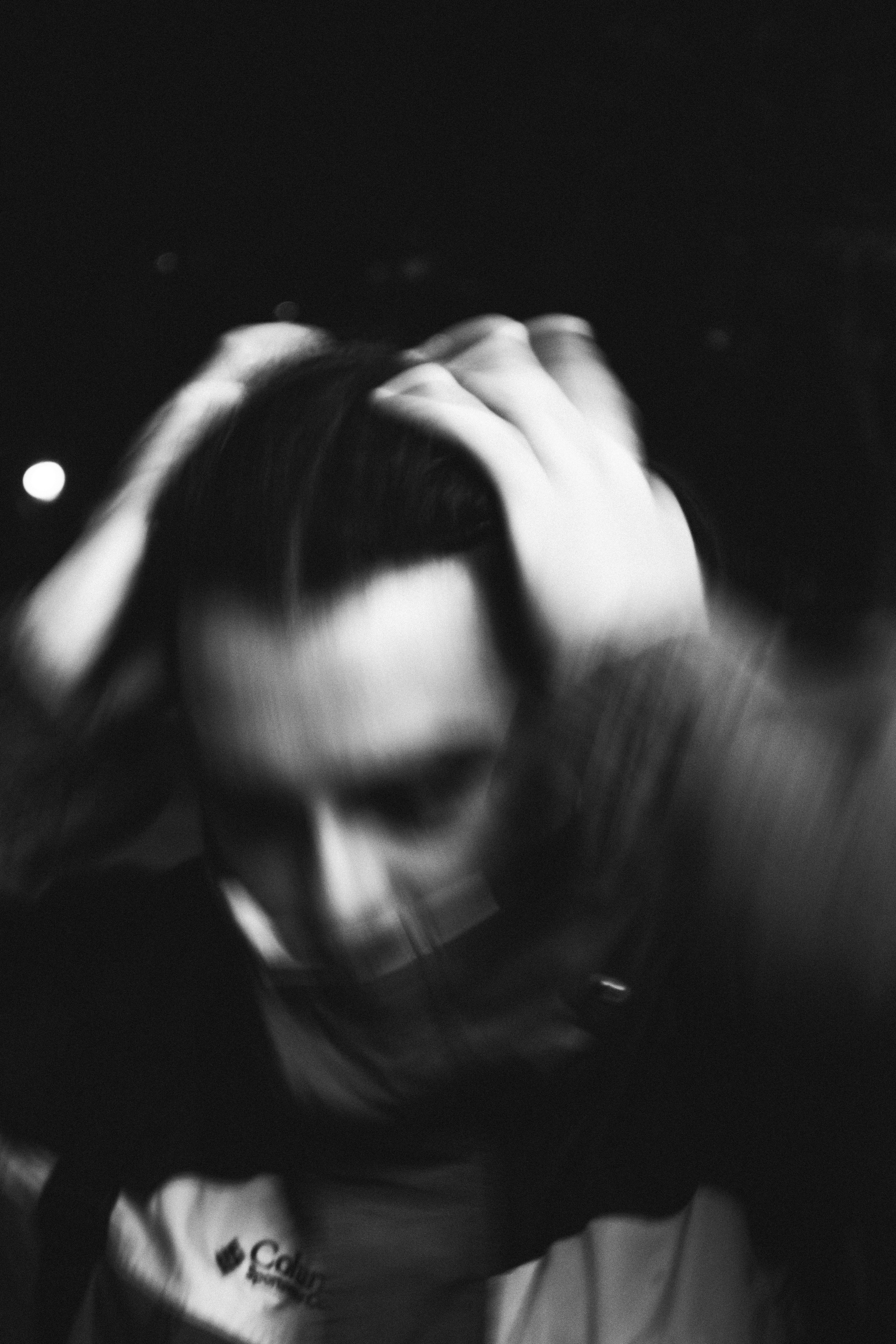 A black and white image of a person with their hands on on their head from a slightly blurred perspective