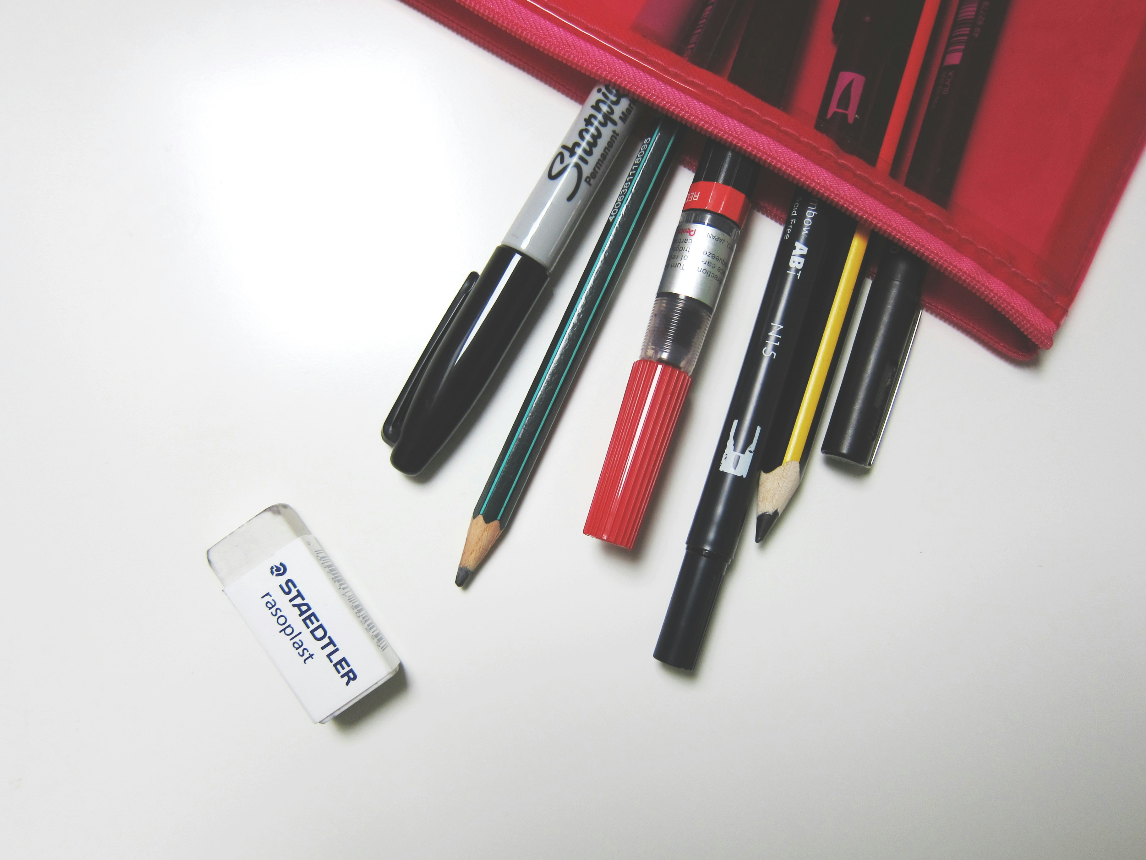A number of pens and pencils fallen out of a red mesh pencil case
