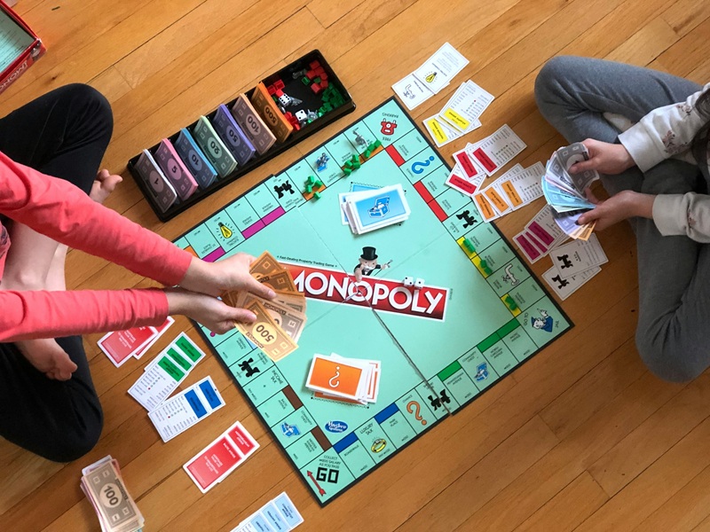 Twp people sitting on a wooden floor playing Monopoly board game
