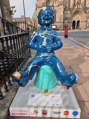 Sculpture in street of boy laughing, sitting on an upturned bucket.