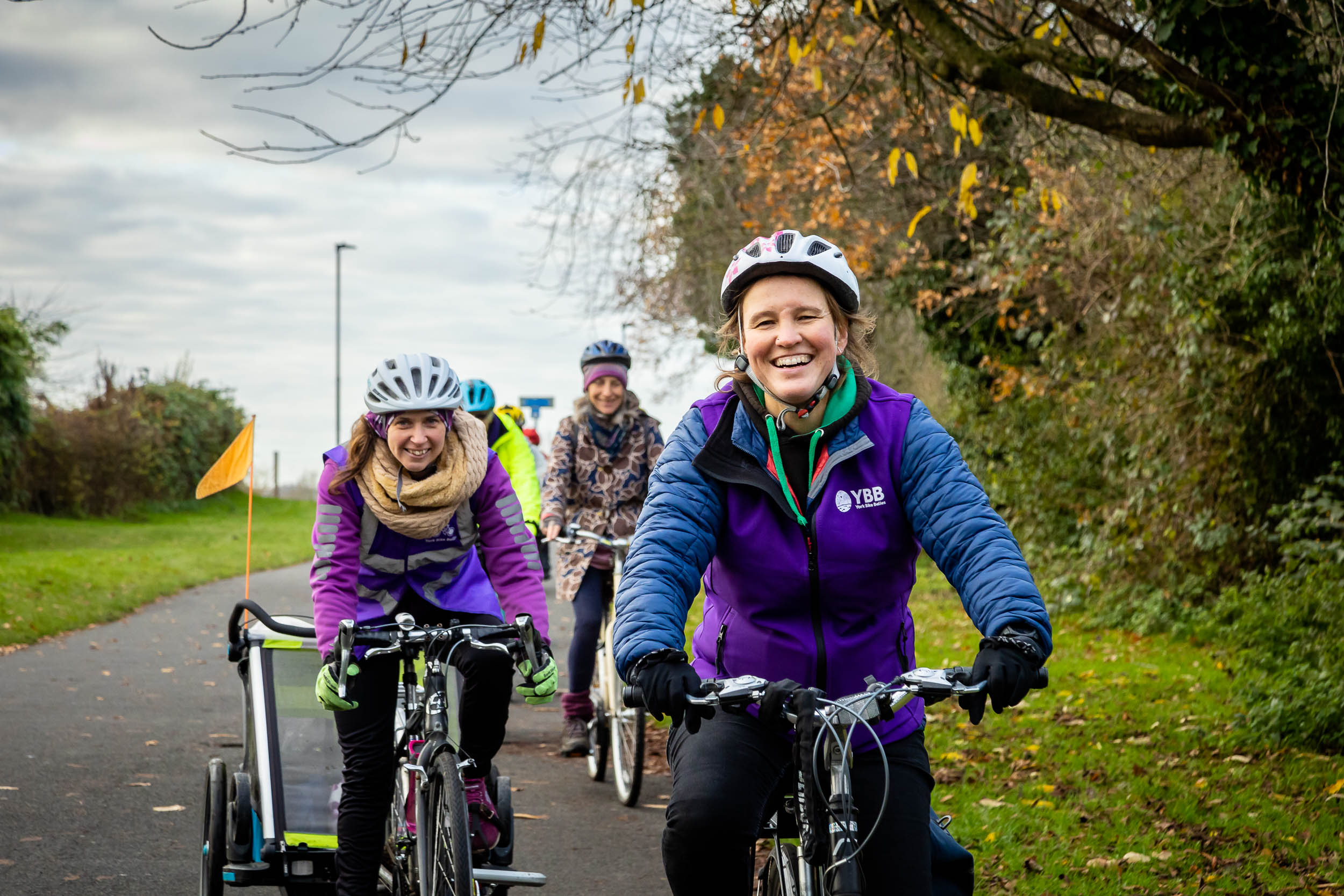 Three people on bikes are smiling as they cycle along a cycle path towards the camera.
