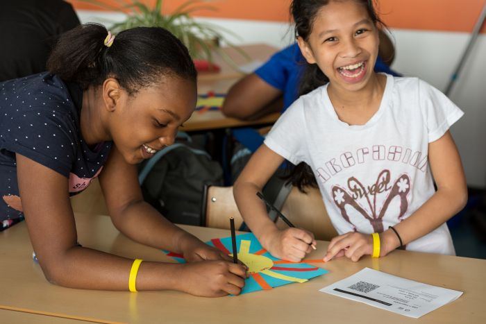 Two young girls working together at a school desk.