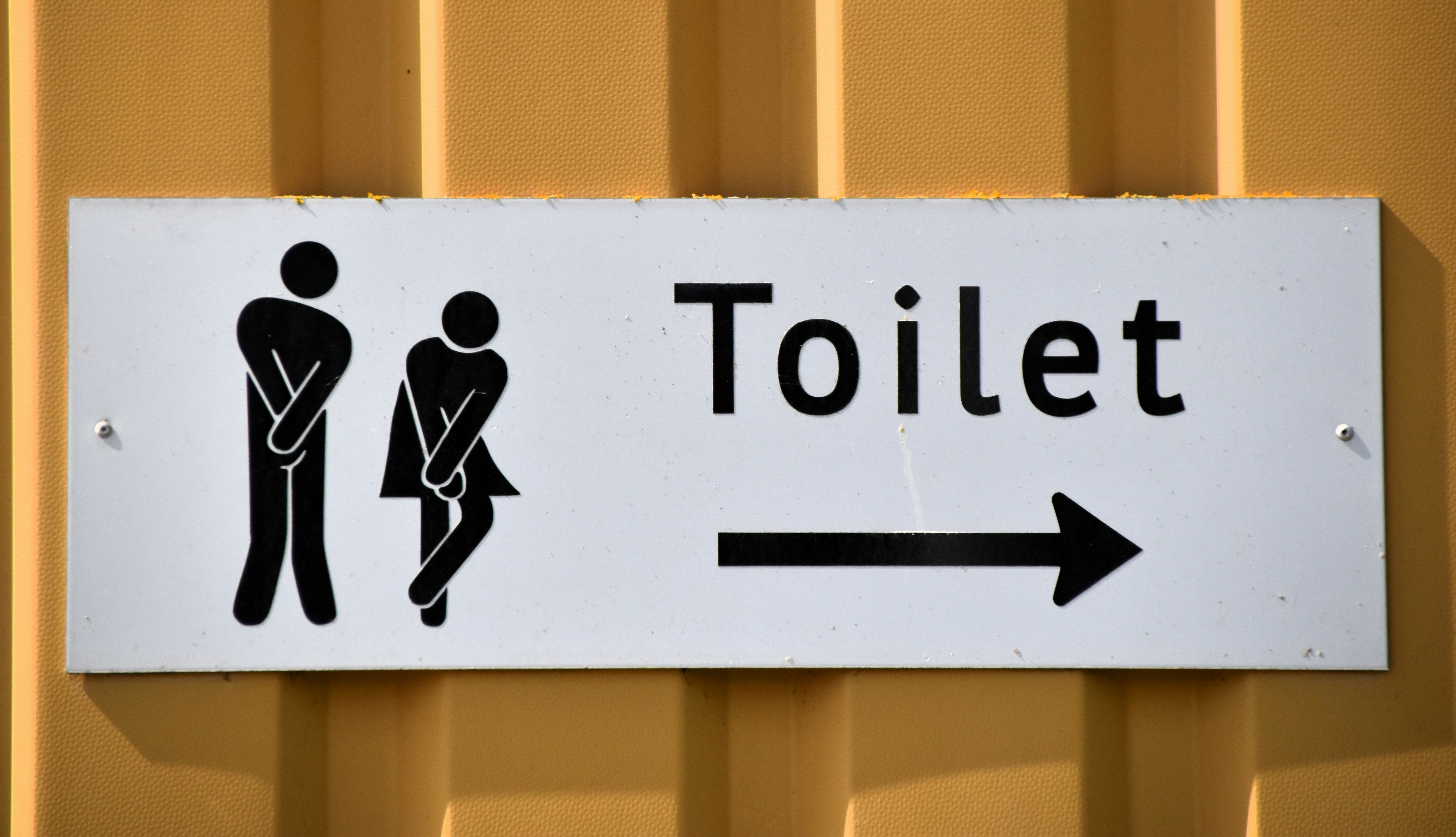 Toilet sign on a yellow background. The sign utilizes two stick figures, one stylized as male and one a female.