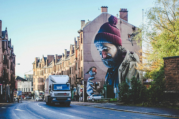 A photo of a city street scene with a large mural on the end of a building.